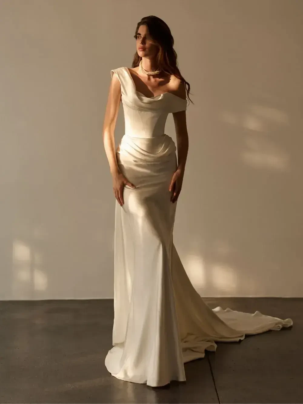 A model wearing a form-fitting, elegant white gown with off-shoulder sleeves, posed against a neutral background.