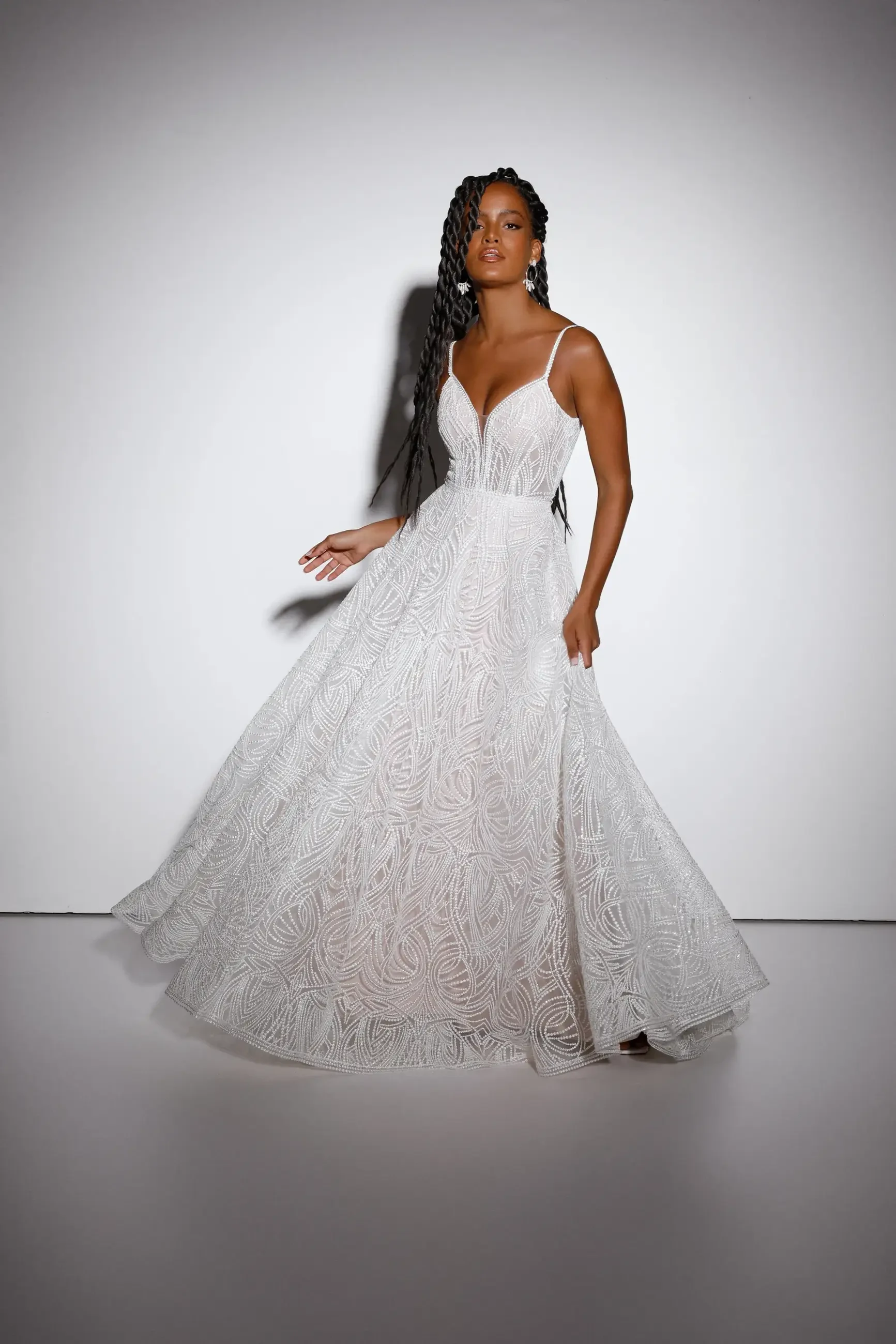 A woman in a white gown with intricate patterns poses elegantly.