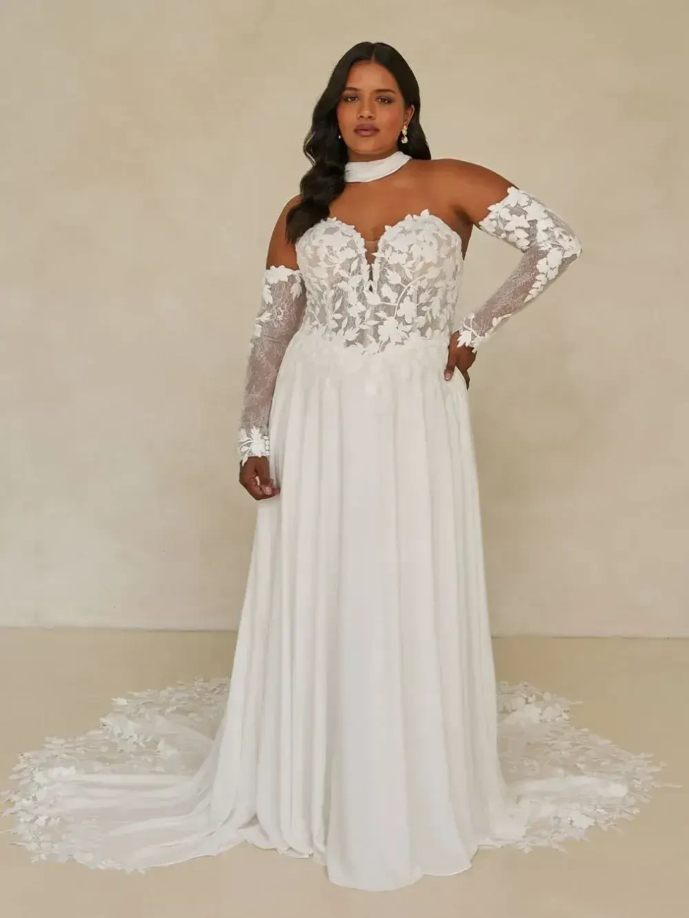 A woman wearing a white wedding dress with intricate lace details and long, sheer sleeves.